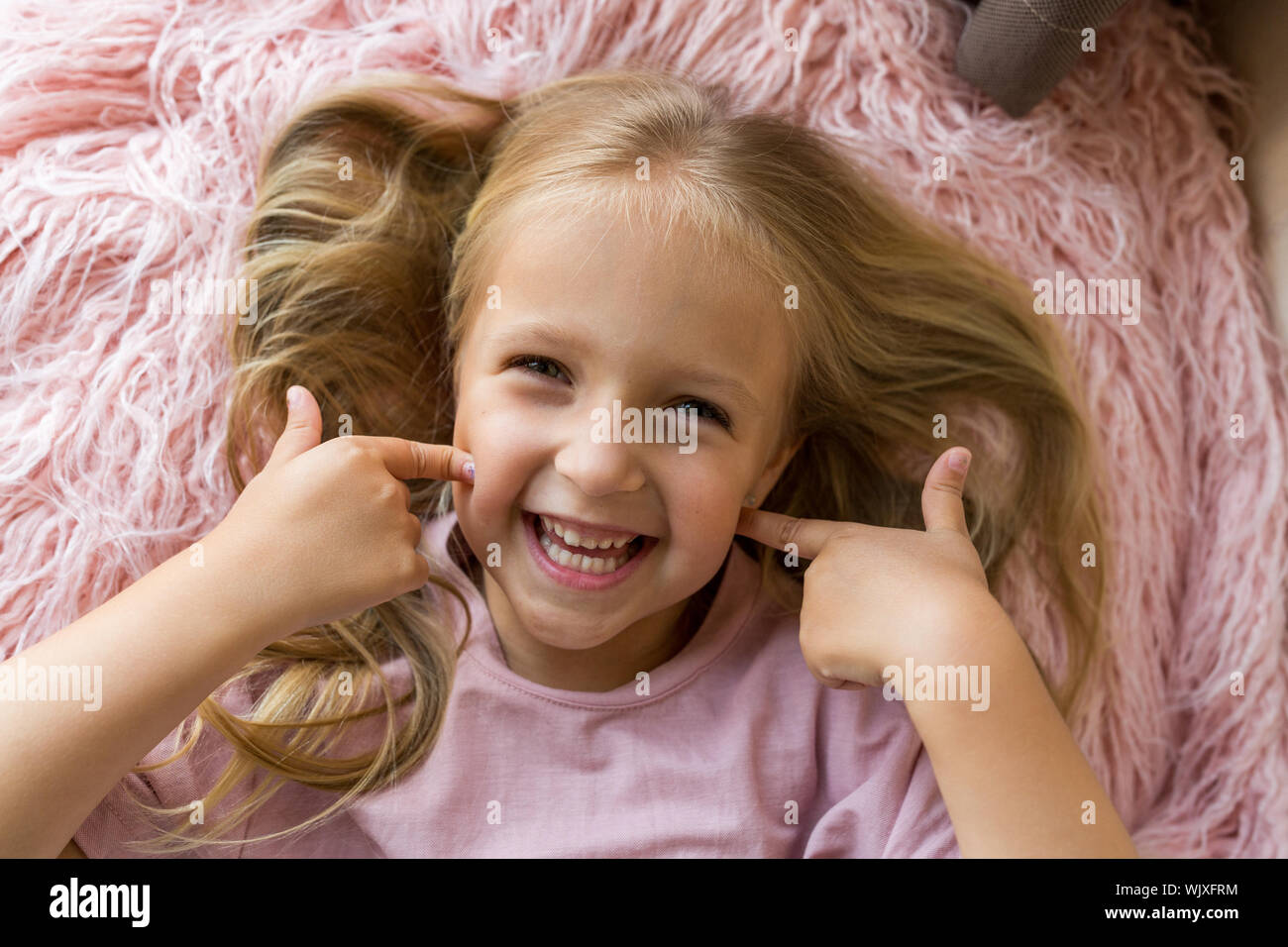 Adorable Little Girl With Long Blonde Hair Lying On Pink Fur