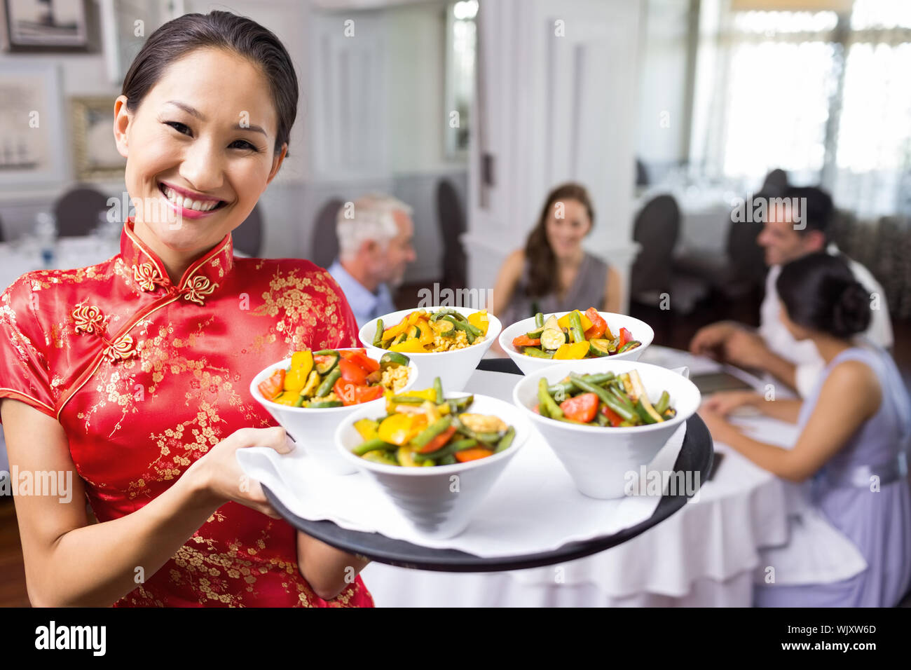 Portrait of a waitress carrying food tray with people sitting at dining