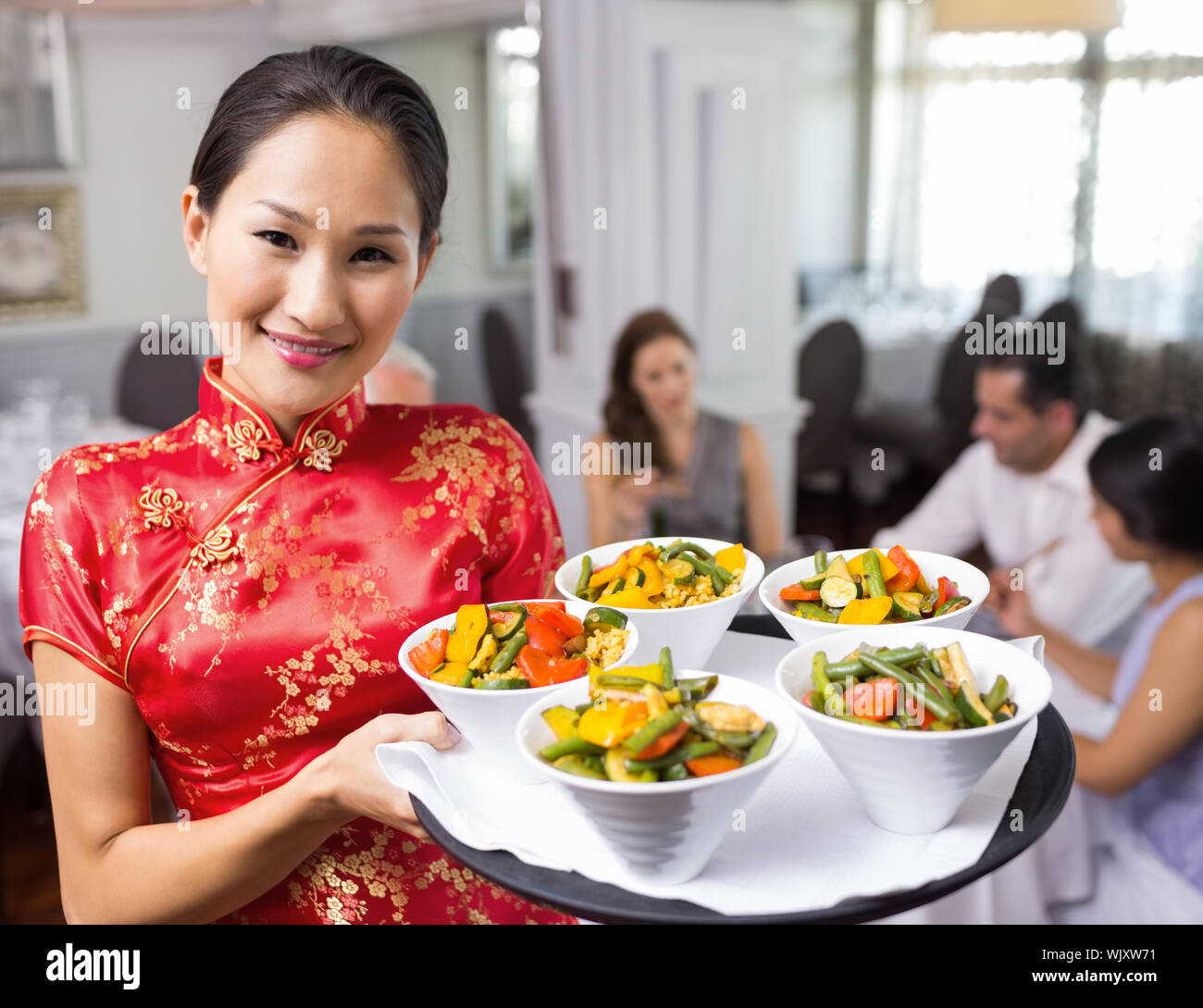 Portrait of a waitress carrying food tray with people sitting at dining table in restaurant
