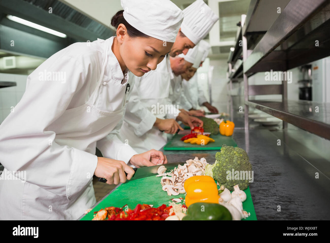 Row of trainee chefs slicing vegetables in a commercial kitchen Stock Photo