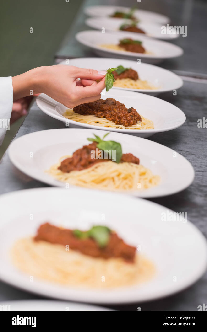 Chef putting basil leaf on spaghetti dish in a commercial kitchen Stock