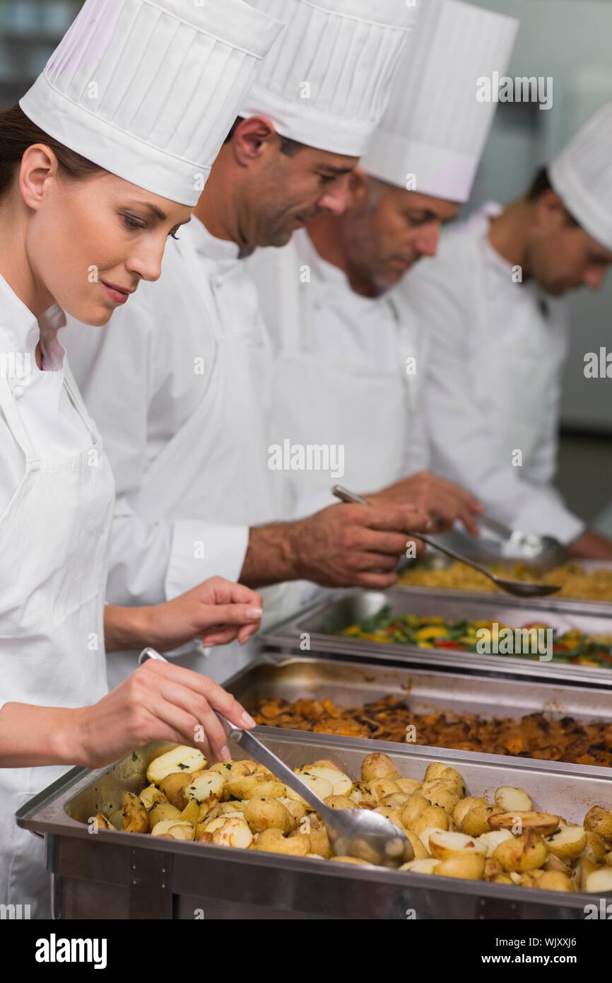 Chefs serving hot food from serving trays in a commercial kitchen Stock