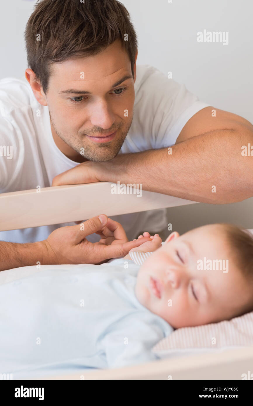 Happy father watching over baby son in crib at home in bedroom Stock Photo