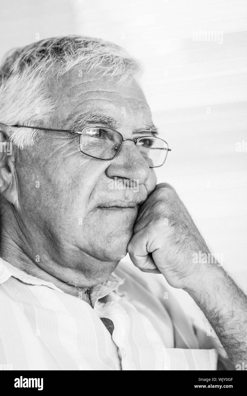 Thoughtful senior man sitting on the couch at home in the living room Stock Photo