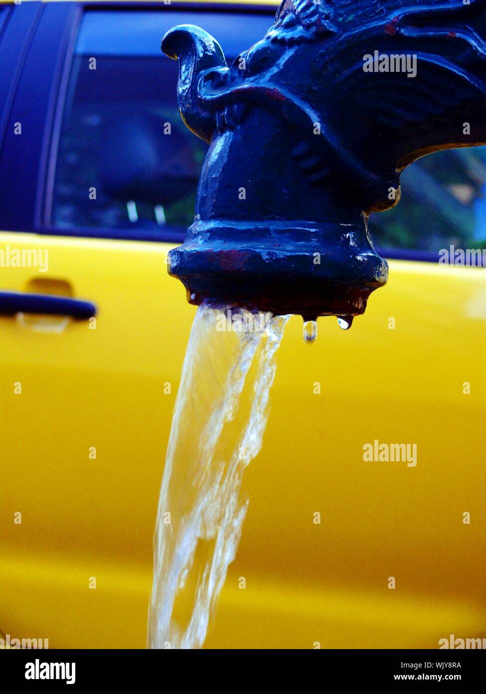 Close Up Of Water Falling From Faucet Against Yellow Car Stock
