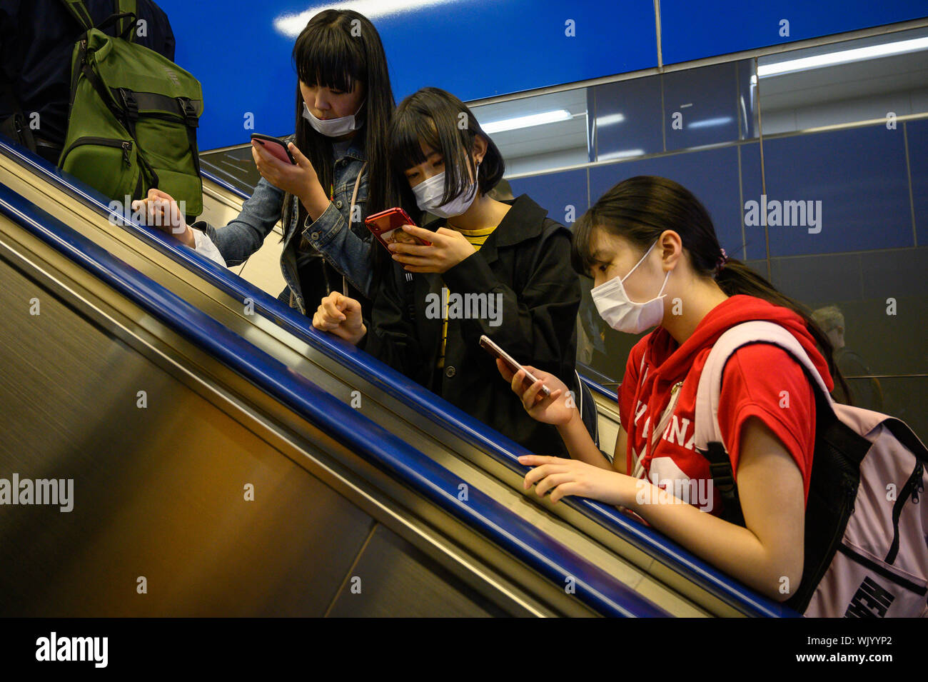 Young Japanese women looking at their mobile phones on an escalator in the Tokyo Metro, Tokyo, Japan Stock Photo