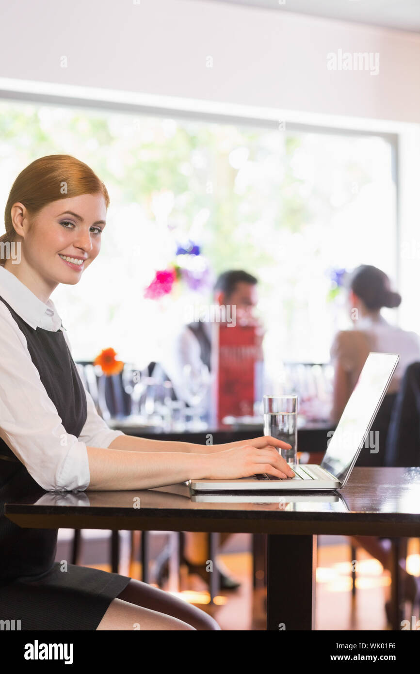 Attractive businesswoman working on laptop smiling at camera Stock Photo