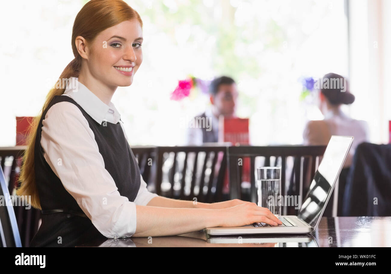 Smiling businesswoman working on laptop looking at camera Stock Photo
