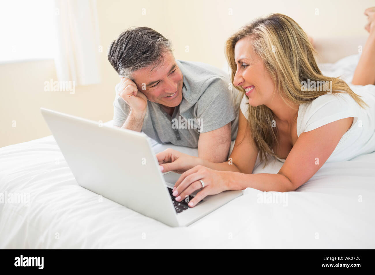Laughing couple lying on bed using a laptop Stock Photo