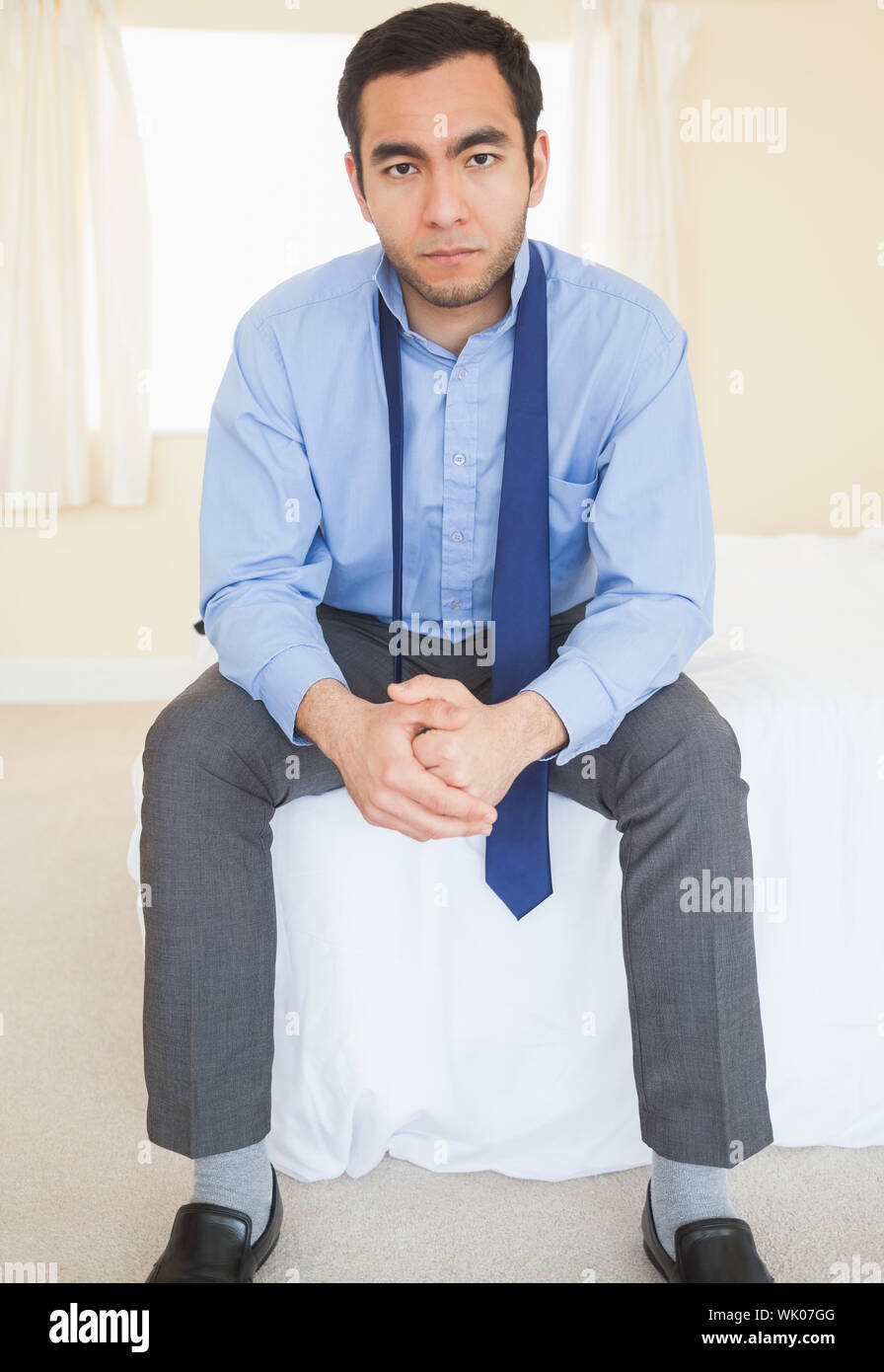 Unsmiling man sitting on his bed Stock Photo