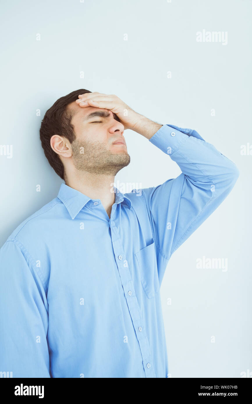 Upset man eyes closed and a hand on the forehead leaning against a wall ...