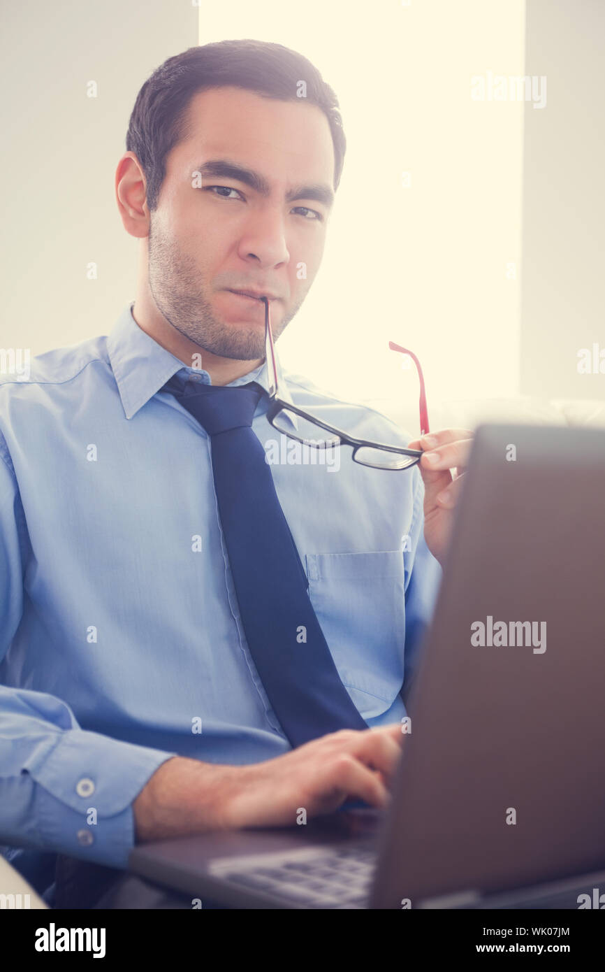 Irritated man biting his eyeglasses and using a laptop Stock Photo