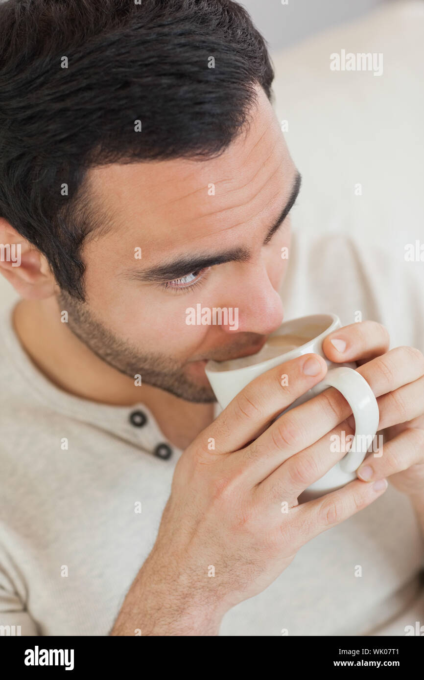 Thoughtful handsome man drinking coffee while relaxing on sofa Stock Photo