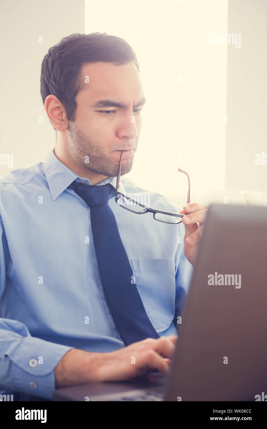 Focused man biting his eyeglasses and using a laptop Stock Photo