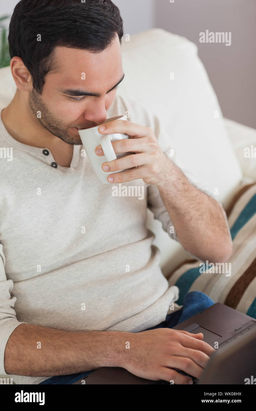 Peaceful attractive man drinking coffee while using his laptop Stock Photo