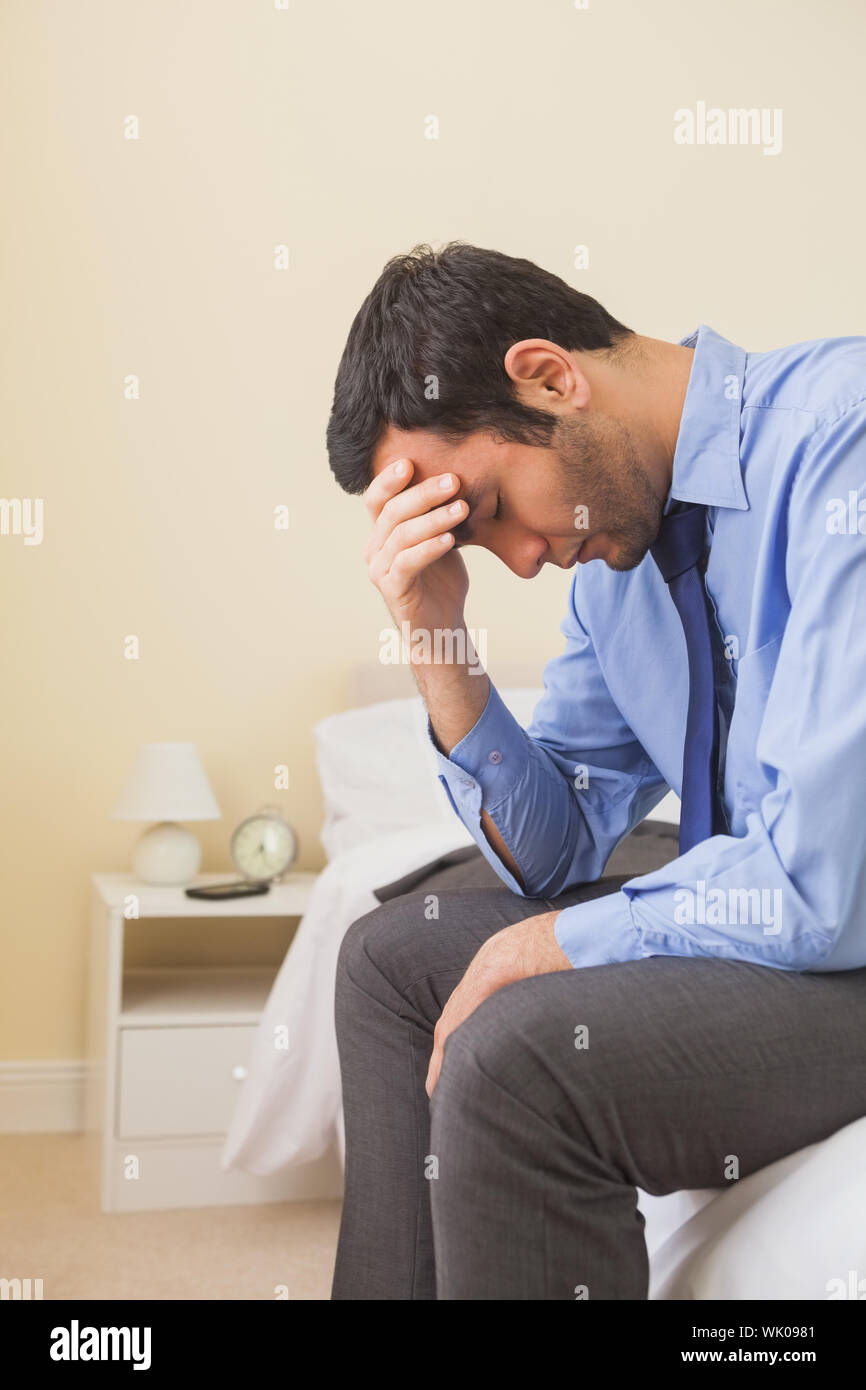 Upset man sitting head in hands on his bed Stock Photo