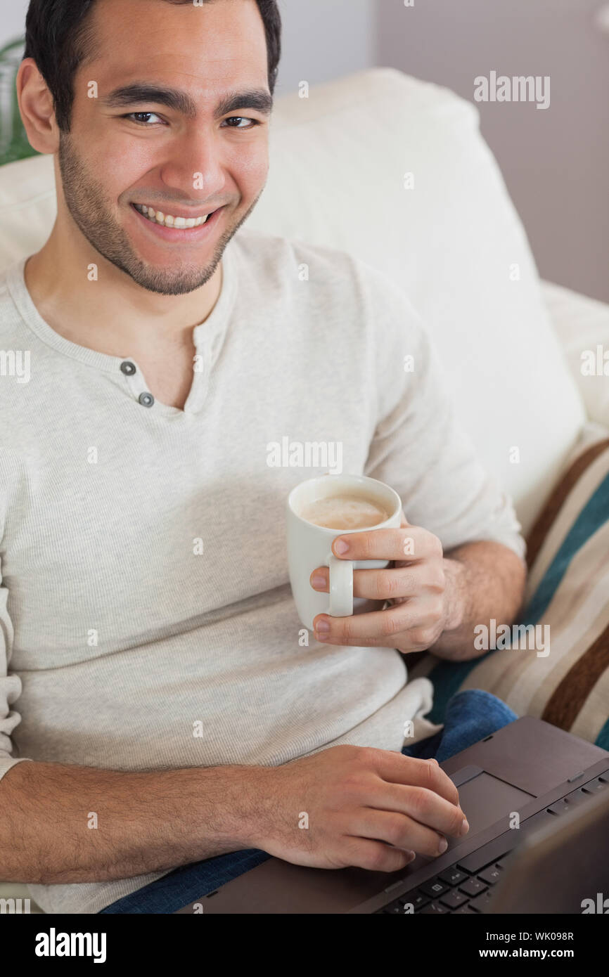 Smiling attractive man drinking coffee while using his laptop Stock Photo