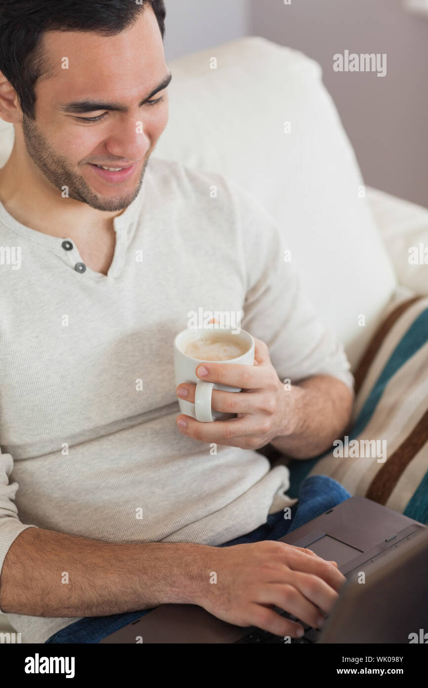 Calm attractive man drinking coffee while using his laptop Stock Photo