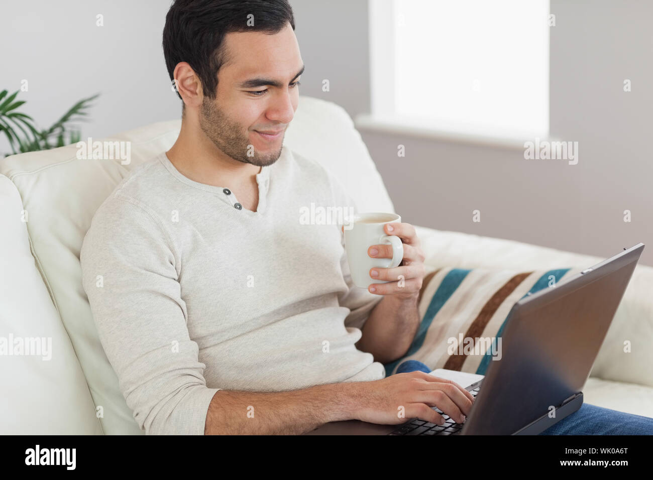 Calm attractive man drinking coffee while working on his laptop Stock Photo