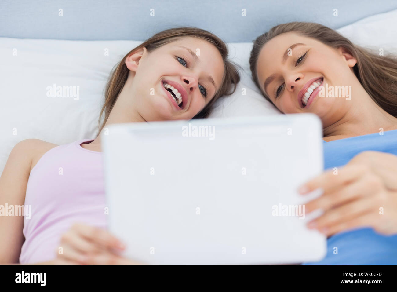 Happy girls lying in bed holding tablet Stock Photo Alamy