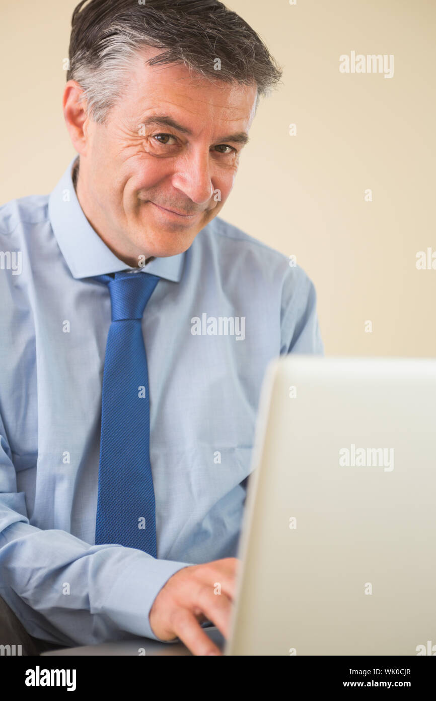 Pleased man using a laptop sitting on bed Stock Photo