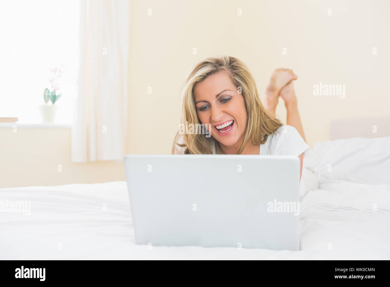 Laughing woman using a laptop lying on her bed Stock Photo