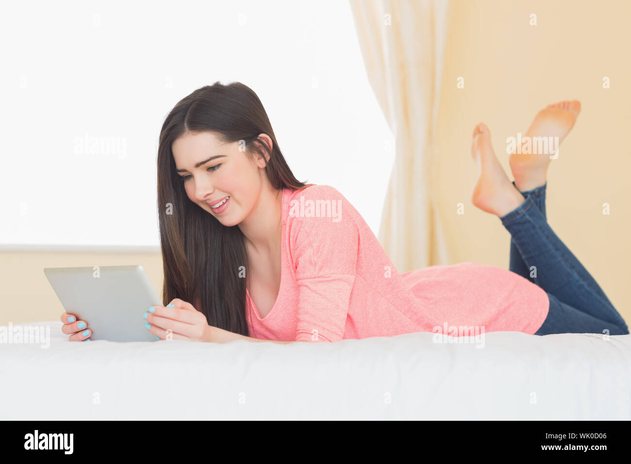 Smiling girl looking and using a tablet pc laying on a bed Stock Photo ...