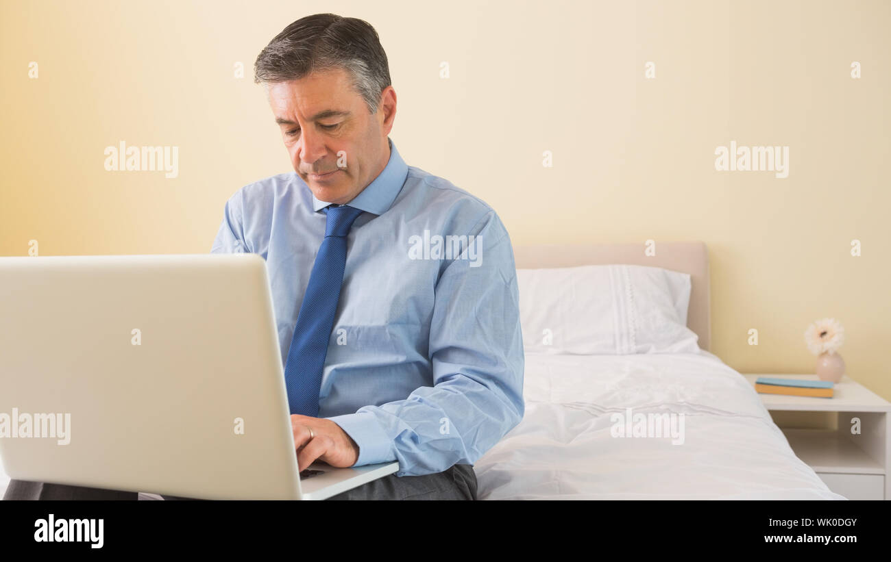 Thoughtfulman using a laptop sitting on a bed Stock Photo