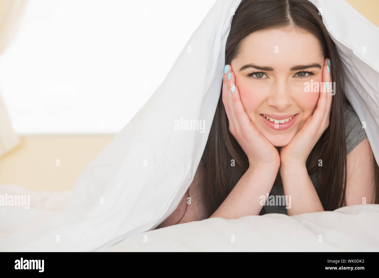 Happy girl looking at camera lying in her bed Stock Photo - Alamy