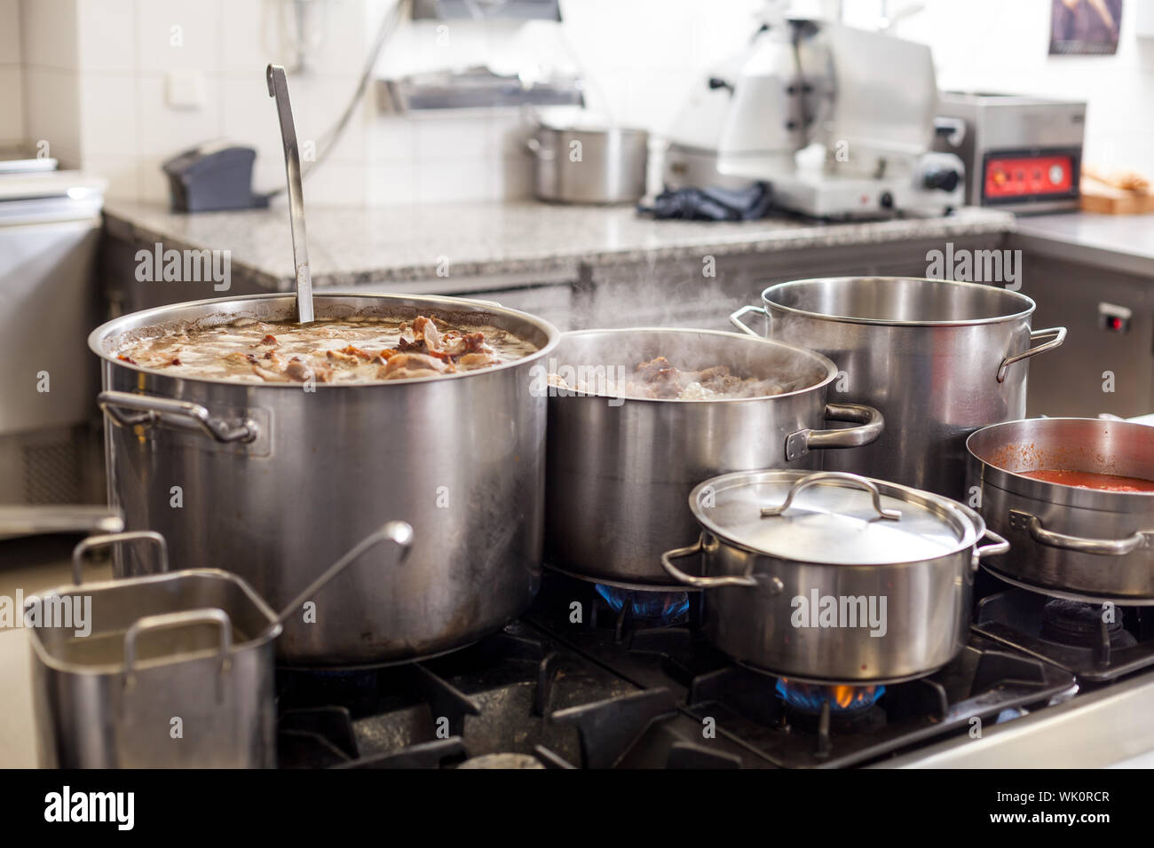 https://c8.alamy.com/comp/WK0RCR/cooking-in-a-commercial-kitchen-with-large-stainless-steel-pots-filled-with-stew-and-vegetables-on-a-central-gas-hob-WK0RCR.jpg