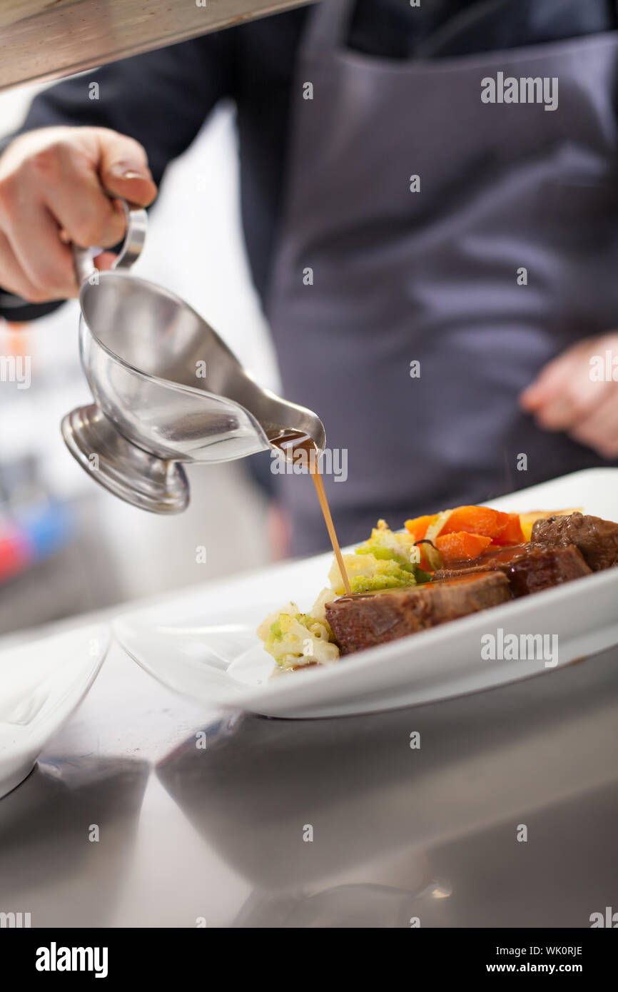 Chef plating up food in a restaurant pouring a gravy or sauce over the ...