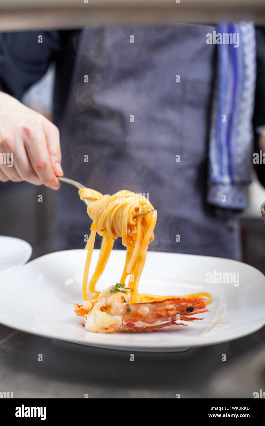 Chef plating up seafood pasta placing spaghetti twirled around a fork