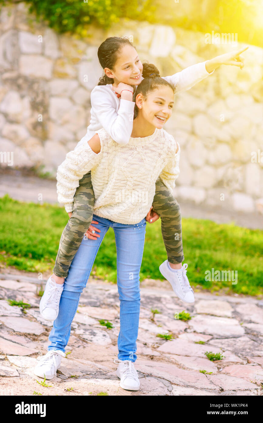 Two Young Teenagers Playing A Game Together At Sunny Day. Best Friends Having Fun In The Summer Riding each other's back. Young girl showing something. Stock Photo