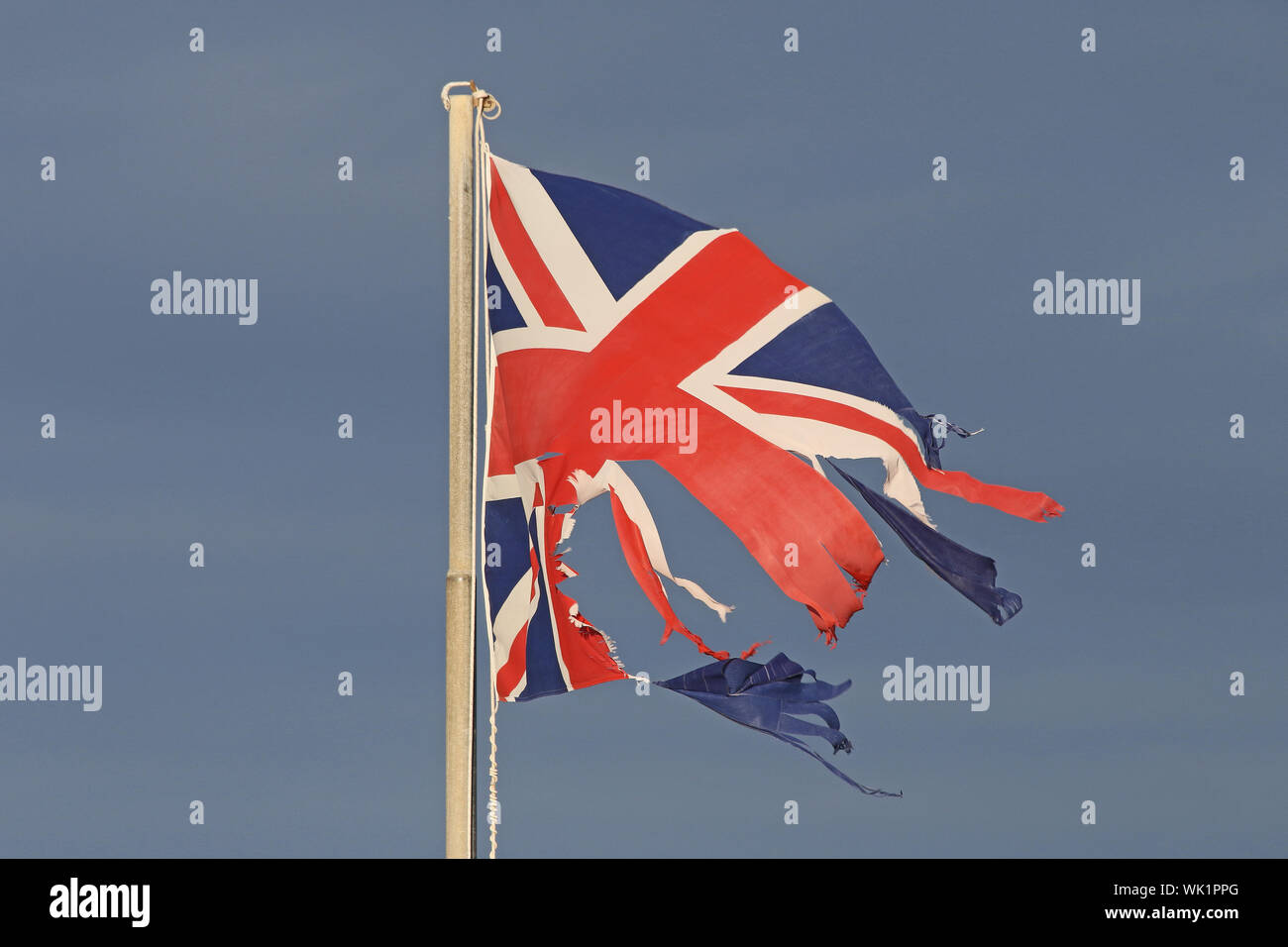 British flag or Union Jack torn and tattered flying in the winter by the sea in Italy representing the disaster of Brexit Stock Photo
