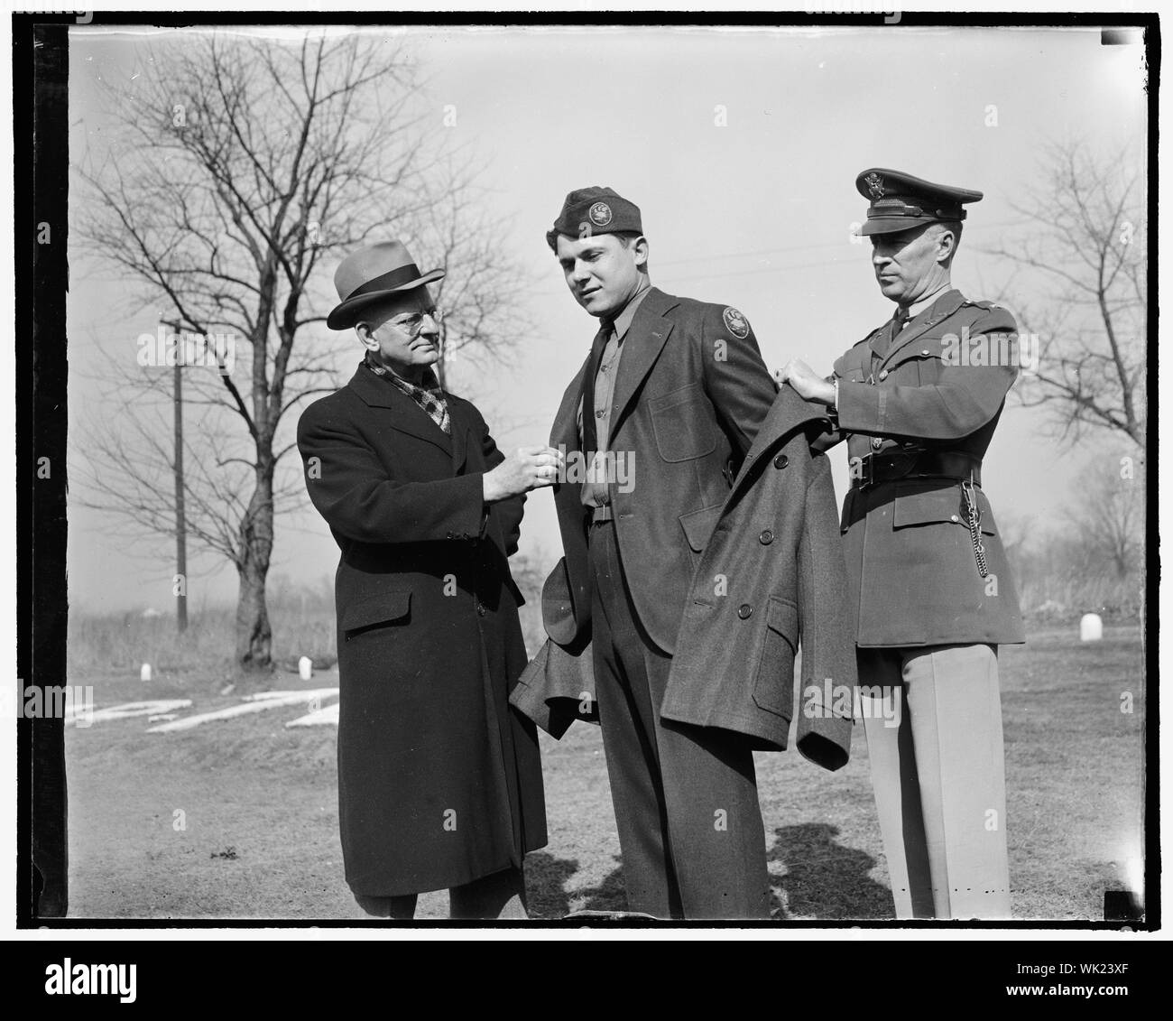 Inspects new CCC uniform. Washington, D.C., Feb. 1. Robert E. Fechner, left, Director of the Civilian Conservation Corps, inspecting the new uniform issued to members of the Corps for the first time today. The outfit consists of a two-button pleated back, sack coat of spruce green topped off with new style overseas cap and a red an yellow CCC insignia on left shoulder. Frank Papuga is wearing uniform while on right is Lt. Col. Thomson Lawrence, in command of Central District, 3rd. corps area Stock Photo