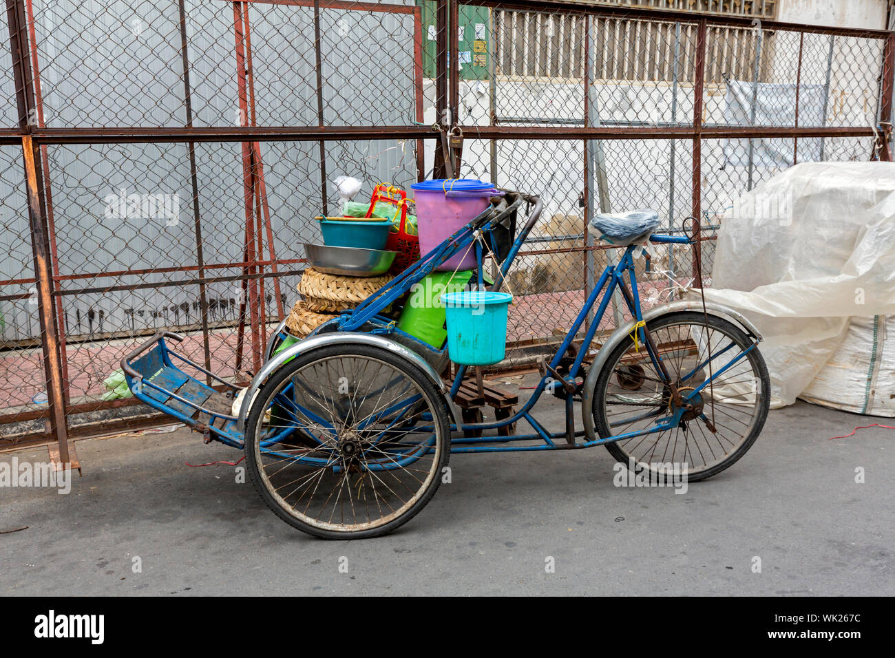 A cyclo loaded with food delivery utensils is parked on a city street while the driver makes a food delivery in urban Phnom Penh, Cambodia. Stock Photo