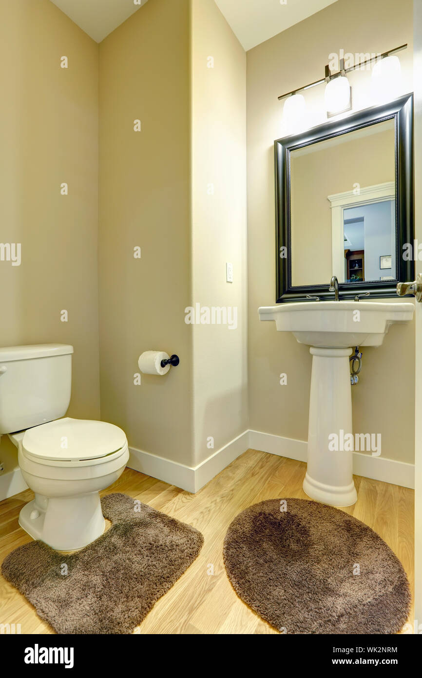 View of small bathroom with white toilet and washbasin stand. Hardwood floor with soft brown rugs Stock Photo