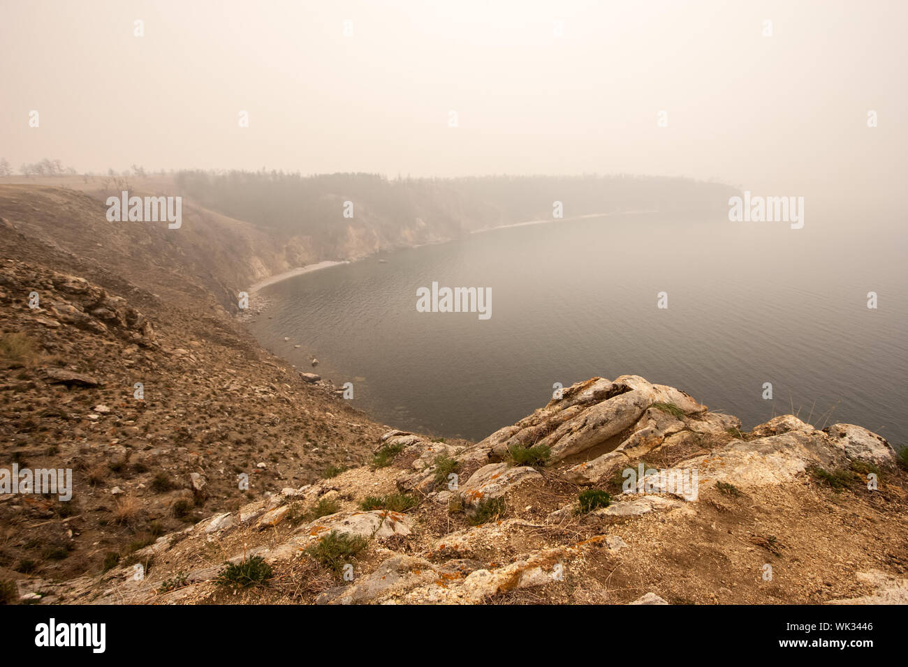 Lake Baikal in the fog in the morning. Shot from a high cliff. Ripples on the water. Selective focus on the front stones. Copy space. Stock Photo