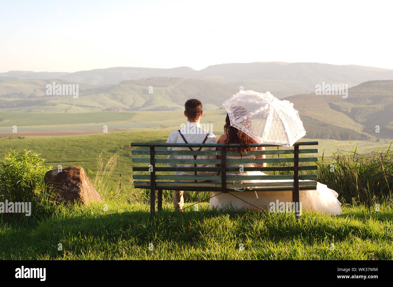 Bride and groom outside garden wedding on bench with African Natal Midlands mountain scenery background Stock Photo