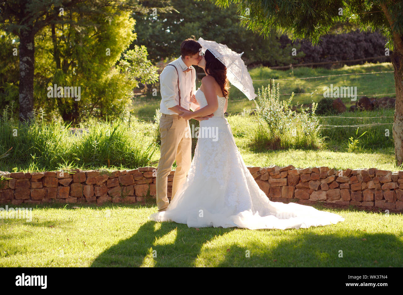 Bride and groom kissing with parasol in outside garden wedding ceremony ...