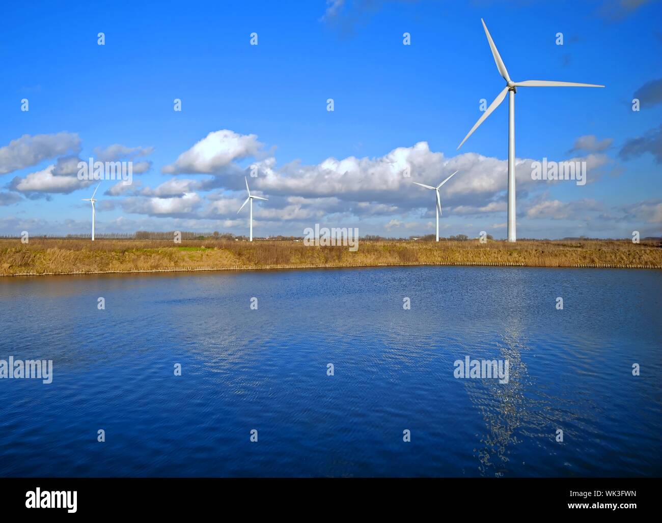 Wind Turbines and lake under a cloudy blue sky Stock Photo - Alamy
