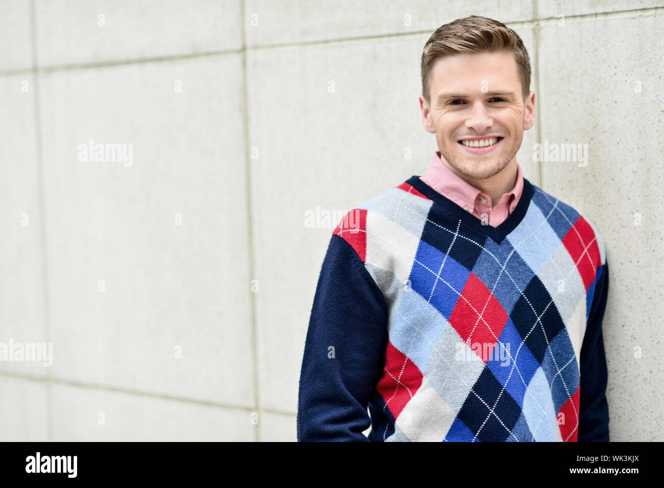 Happy smiling young man leaning against wall Stock Photo - Alamy