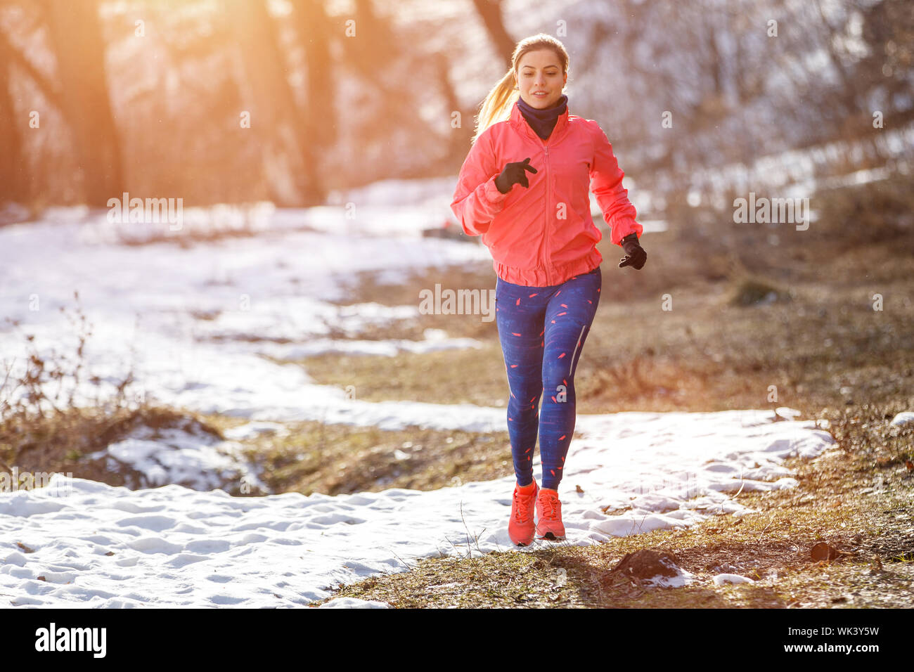 Young slim woman jogging in winter park. Smiling girl running in cold weather Stock Photo