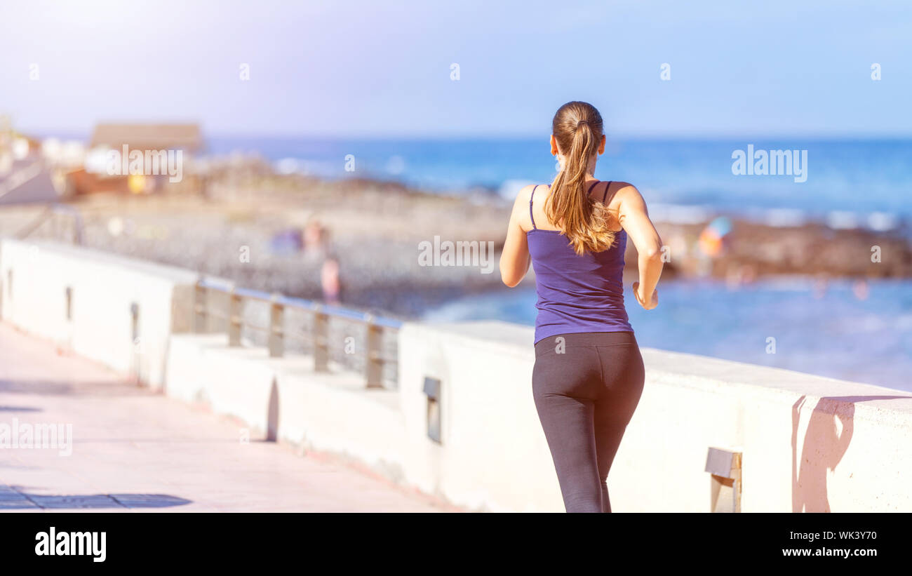 Young sporty woman jogging near the ocean. Back view of running girl with copyspace Stock Photo