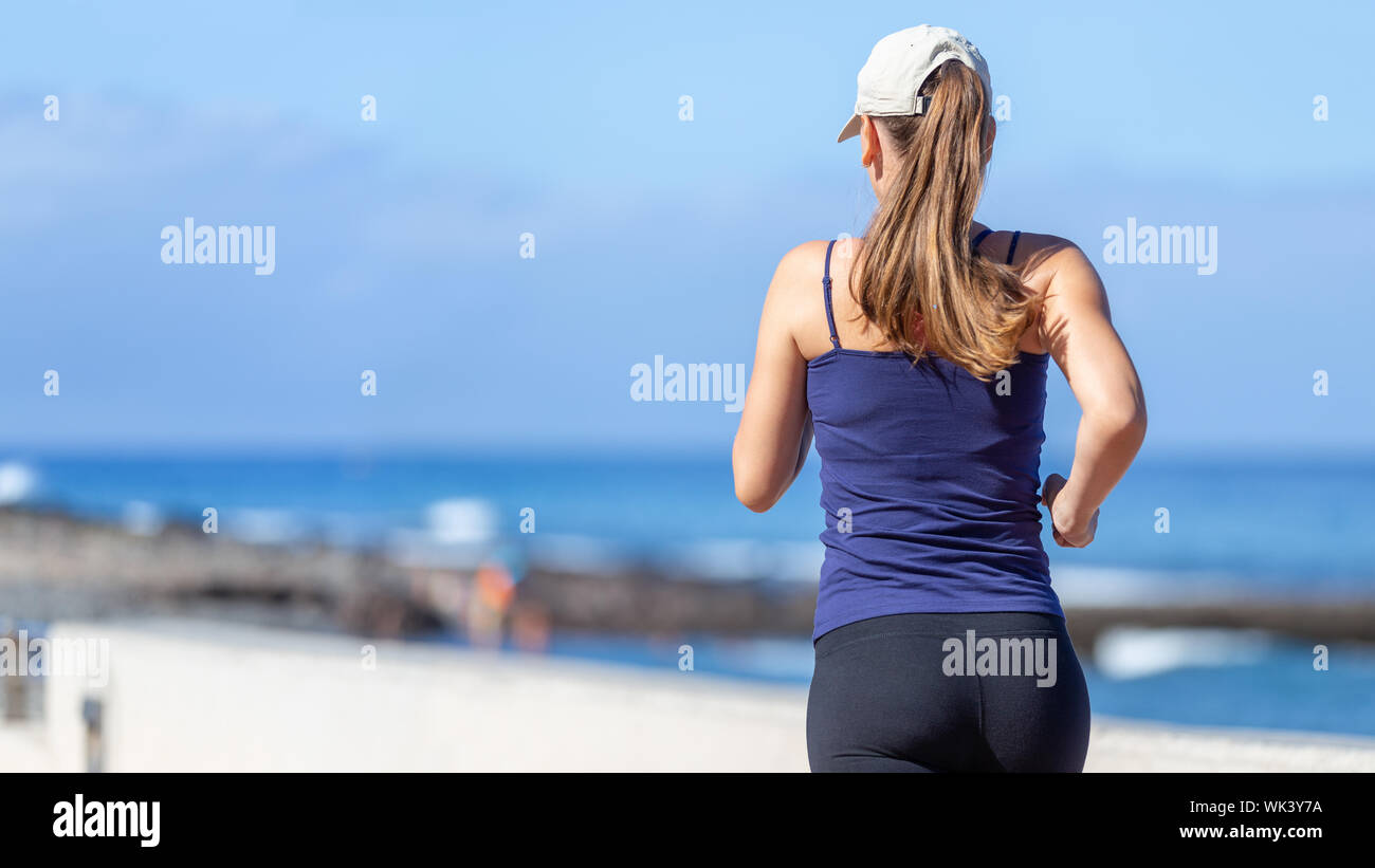 Young sporty woman jogging near the ocean. Back view of running girl with copyspace Stock Photo