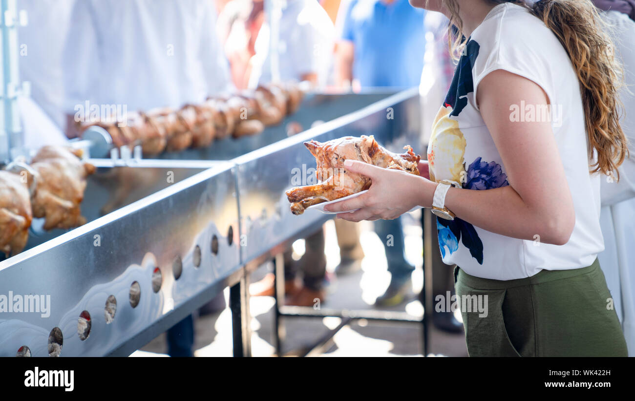 Woman's hand holds a grilled full chicken and many roasted chickens in a row in background. Mengen, Bolu, Turkey. Stock Photo