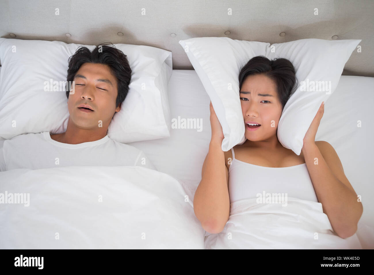 Annoyed woman covering her ears with pillows to block out snoring at