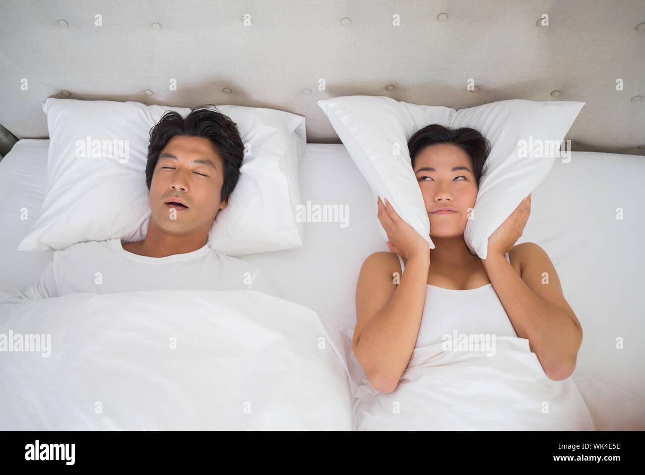 Annoyed woman covering her ears with pillows to block out snoring at