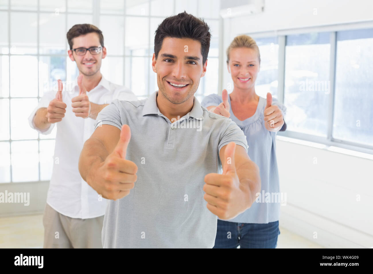 Casual business team smiling at camera with thumbs up in the office ...