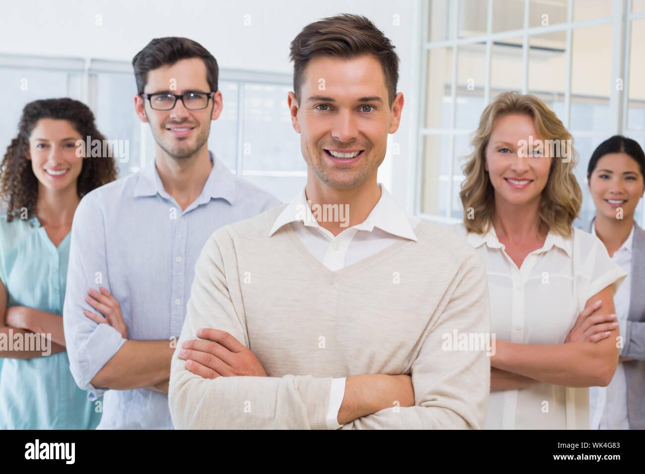 Casual business team smiling at camera with arms crossed in the office ...